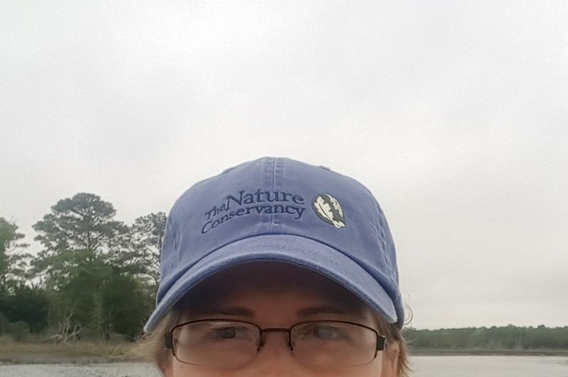 Selfie portrait taken by a woman sitting in a kayak. She is floating in a narrow coastal bay with wetlands and trees behind her.