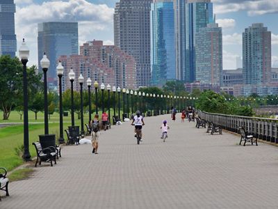 A city sidewalk within a park with trees an d green grass on either side.