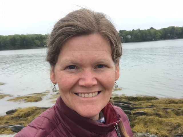 A selfie of Jessica Rice-Healey in front of a rocky shoreline.