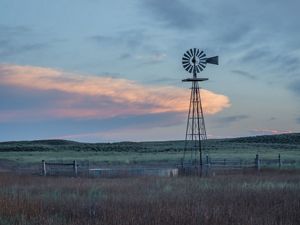 A windmill on grass with sunset in the sky.