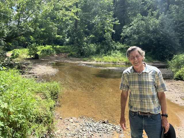 Jon Cannon stands in front of a low creek and forest.