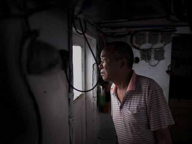 A man looking out a window of a fishing boat.