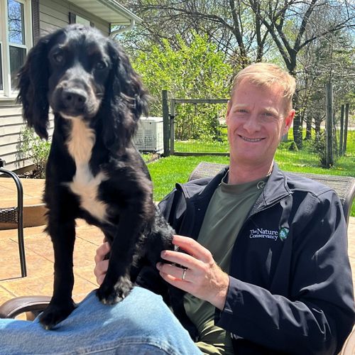 Candid photo of Jeff Walk, Leveraging Our Lands Director for TNC's Midwest Division, with his small black dog on his lap.