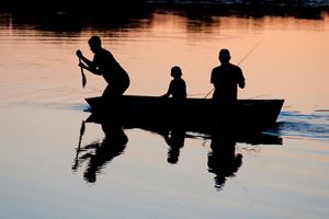 Three people sit in a canoe. One person paddles, one person sits in the middle, and the third person fishes.