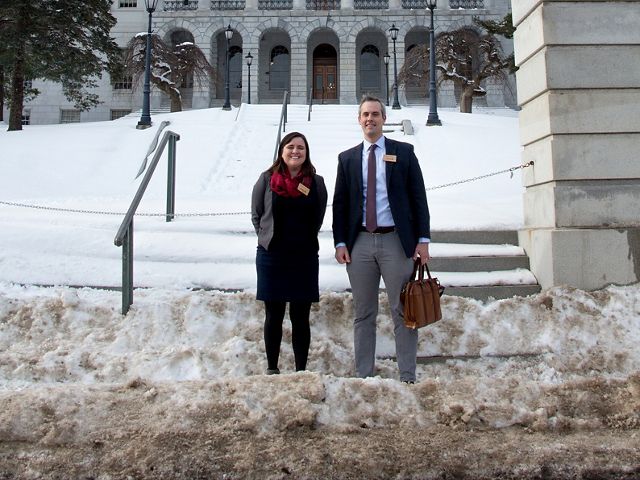 Kaitlyn Nuzzo and Rob Wood stand in front of the Maine State House on a snowy day.