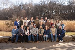 Group photo of about 20 staff members sitting and standing outside with forest in the background.