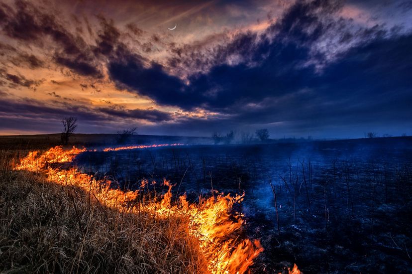 burning line of grass on a prairie with smoke and a crescent moon