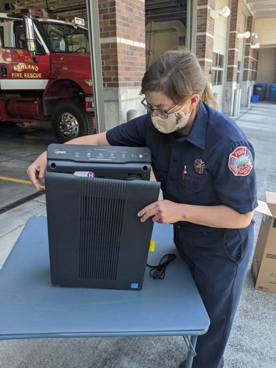 A woman firefighter in station clothes inspects an air purifier outside the Ashland, Oregon, fire station.