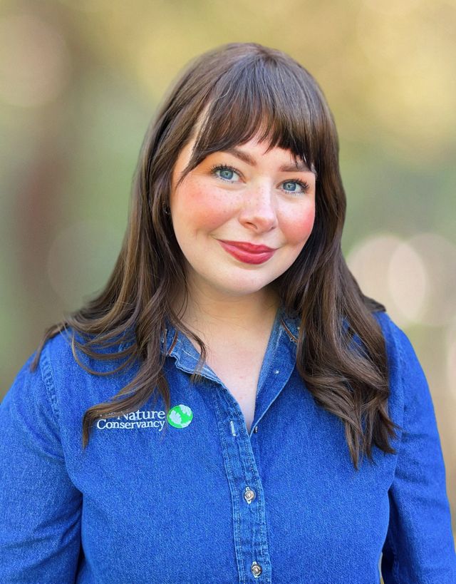 Katie Roby wears a denim TNC shirt and smiles at the camera. 