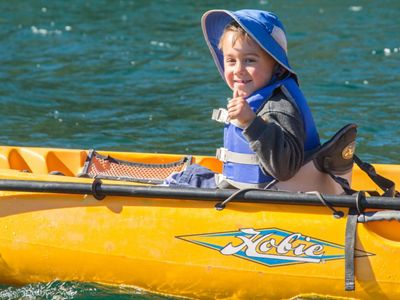 A child wearing a hat rides in a yellow kayak.
