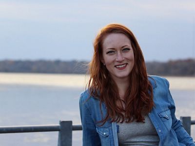 Kayla Wandsnider sits in front of a lake at sunset.