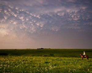 A man on horseback crosses a wide landscape of the Flint Hills of Kansas at dusk.