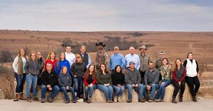 Group photo of about 25 staff members sitting and standing outside with prairie in the background.