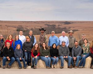 Group photo of about 25 staff members sitting and standing outside with prairie in the background.