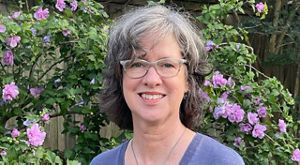 A woman wearing glasses poses next to flowers.