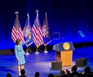 Kathy Hochul, wearing a blue suit, stands on a blue and waves. 