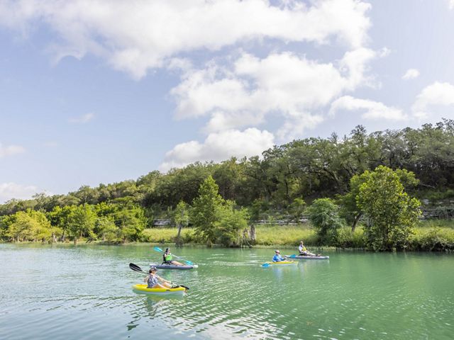 Four kayakers paddle on a blue river.