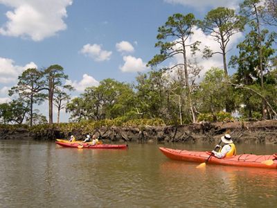 Two red kayaks on a stream with tree-lined banks.