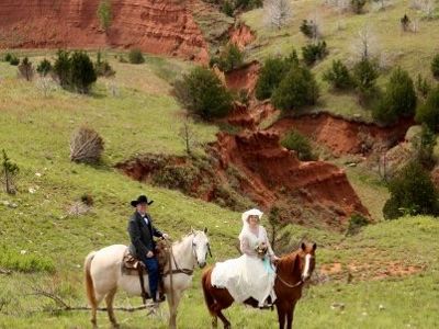 Man and women taking wedding photos on horseback overlooking a ridge crevice shaped like a heart.