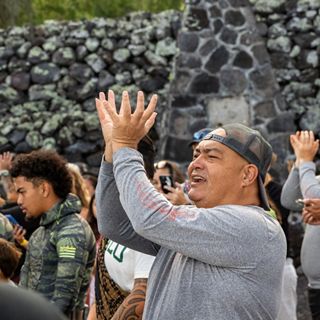 Wearing a gray shirt and baseball cap, Shane Akoni Palacat-Nelsen participates in Hawaiian chant.