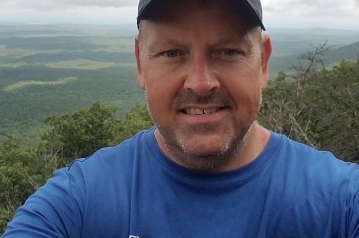 Candid photo of deputy state director Keith Tassin on an overlook of various greenery and clouds in the background..