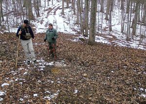 Two people hike using trekking poles, through a snow covered forest in Kentucky. 