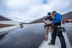 Two solar panel workers look at plans while standing on a roof nearly covered with solar panels.