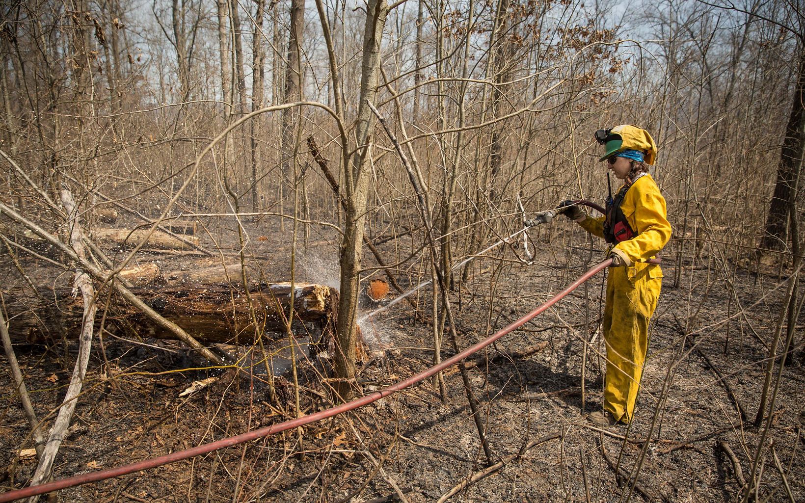 A man in yellow holds a long hose in the woods.