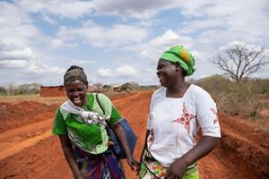 Two women laughing in Kenya while standing on a red clay path. 