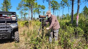 A bearded man with a black tripod and camera.