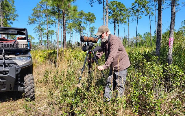 A bearded man with a black tripod and camera.