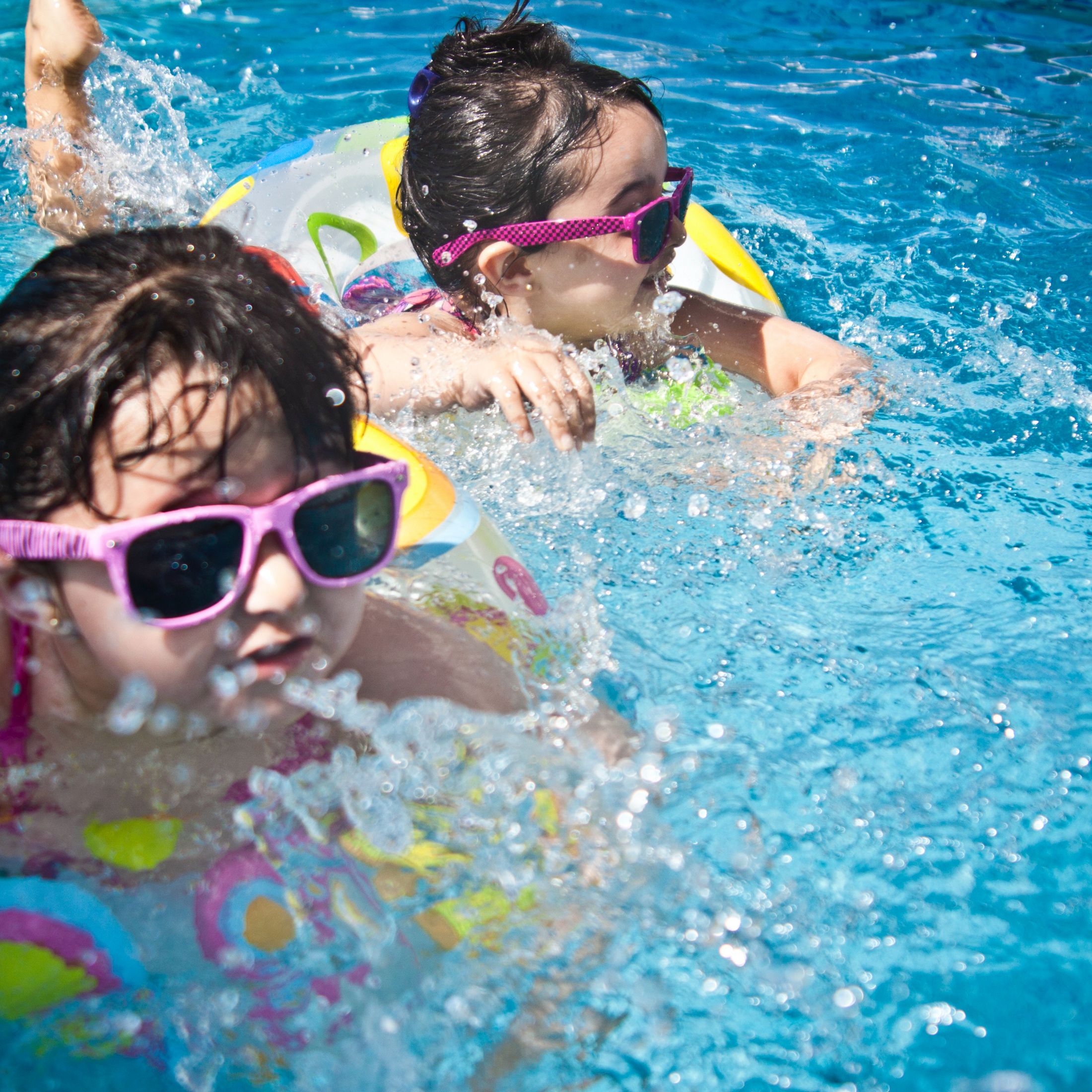 Two young children in swim rings and pink sunglasses floating in a pool.