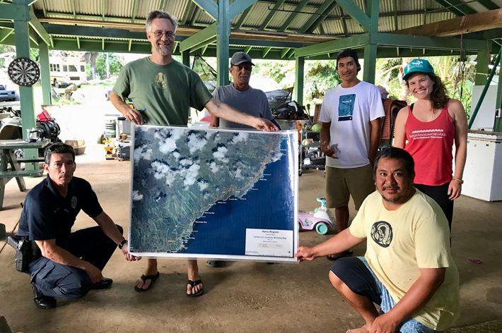 A group of six people pose in an outdoor pavilion holding a large map between them.