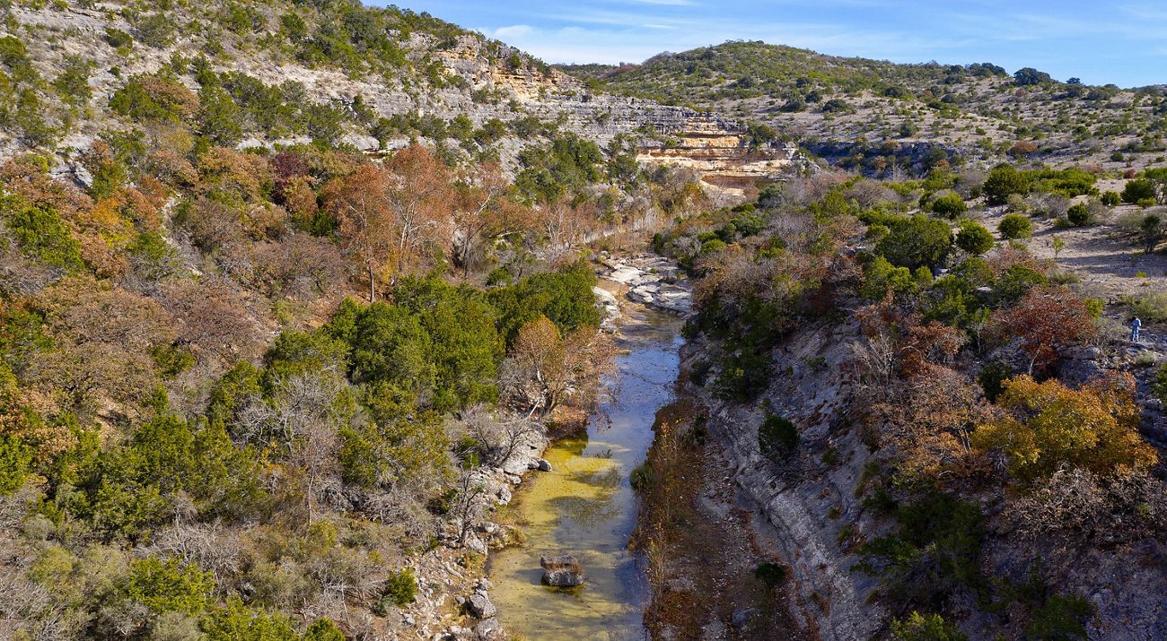 Rocky cliffs covered in brush, cut through by a blue river.