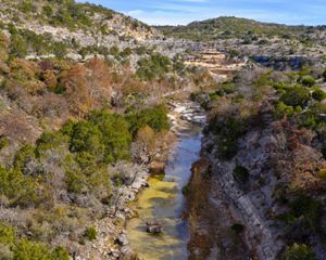 Rocky cliffs covered in brush, cut through by a blue river.