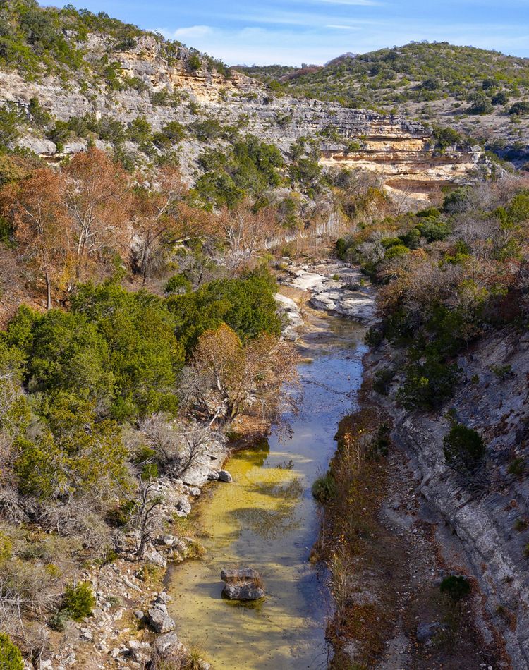 Rocky cliffs covered in brush, cut through by a river.
