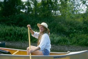 A woman wearing a hat and piloting a canoe.