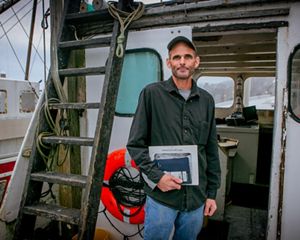 A man stands on the deck of a fishing boat.