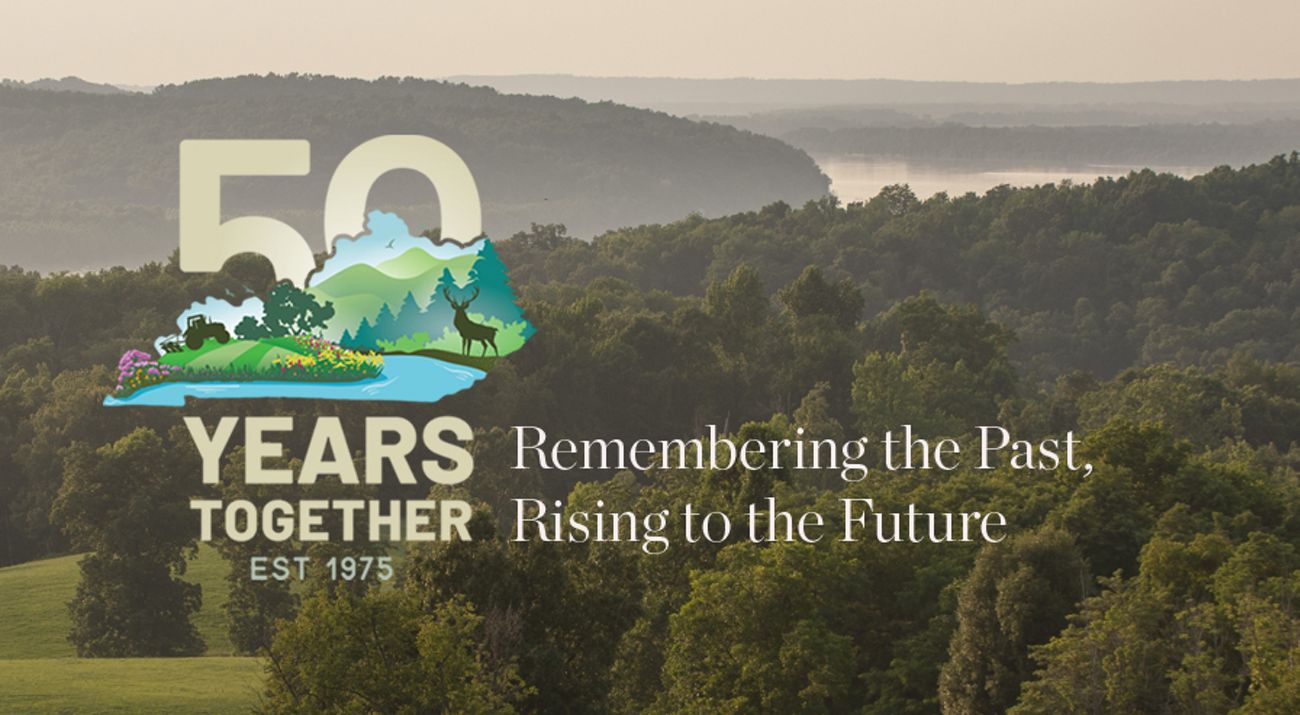 Our TNC in Kentucky 50th Anniversary Logo with a silhouette of Kentucky with animals and plants over it over top of a rolling hill landscape photo.