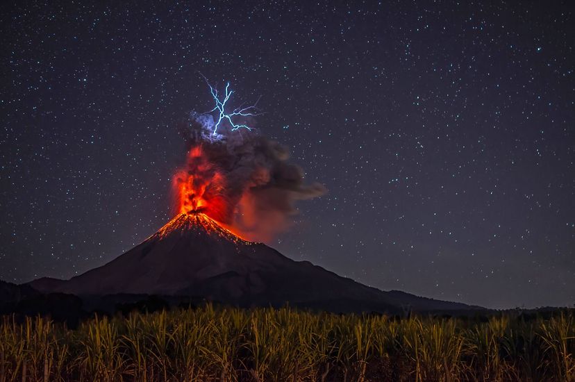 Imagen de un volcano en erupción bajo un cielo nocturno estrellado.