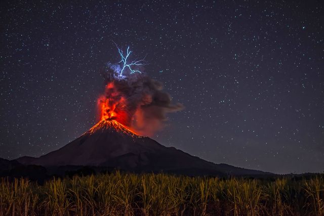 Imagen de un volcano en erupción bajo un cielo nocturno estrellado.