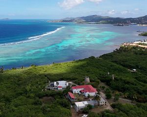An aerial view of a building in a forest along a rocky coastline and the blue ocean.