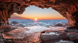Sun sets behind the water of Lake Superior. View from an ice cave as the water rushes over rocks and ice. 