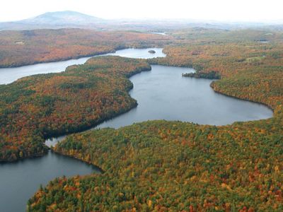 An aerial view of fall colors at a wooded peninsula between two lakes.