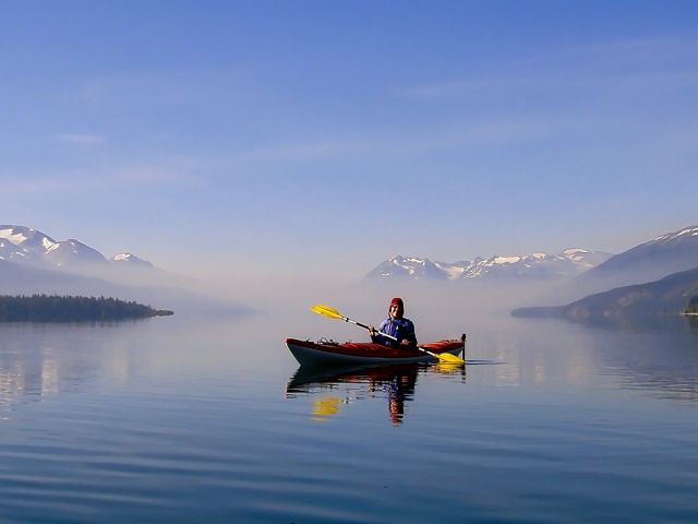 A person in a kayak at Morice Lake, British Columbia, Canada, with distant smoke from a forest fire.