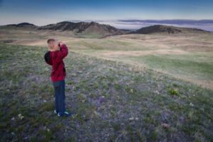 A child holds of pair of binoculars and looks out over the Black Hills landscape.