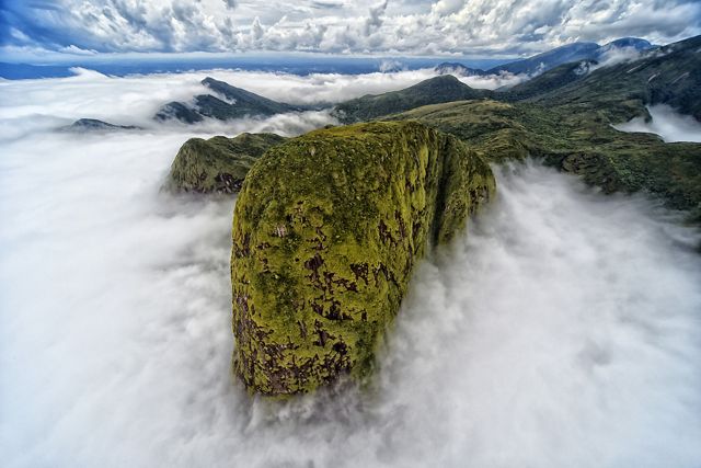 An aerial view of a mountain range emerging above thick clouds.