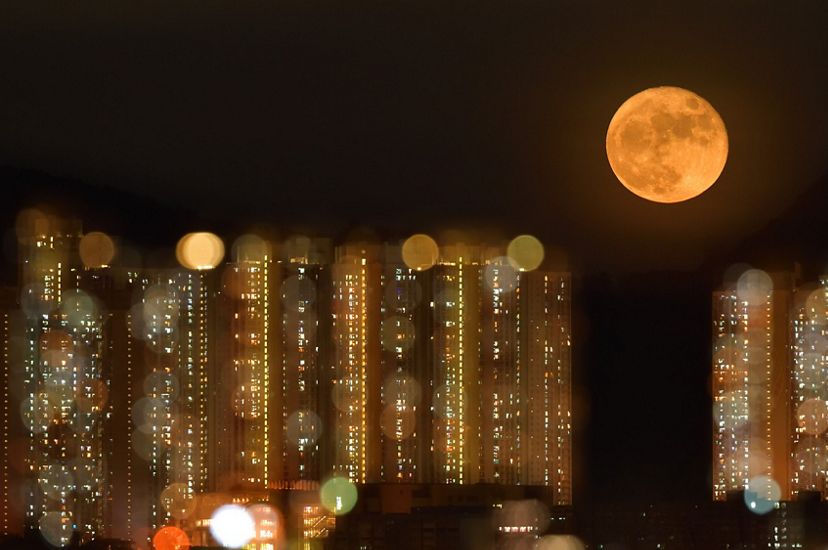 A full moon rises above a bokeh view of highrise buildings in Hong Kong.