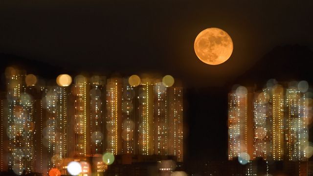 A full moon rises above a bokeh view of highrise buildings in Hong Kong.