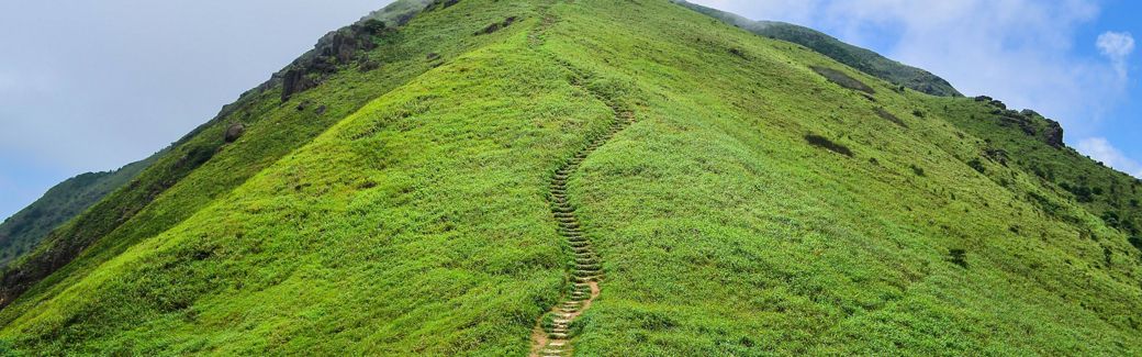 A dirt trail of steps leads up a large green hill.
